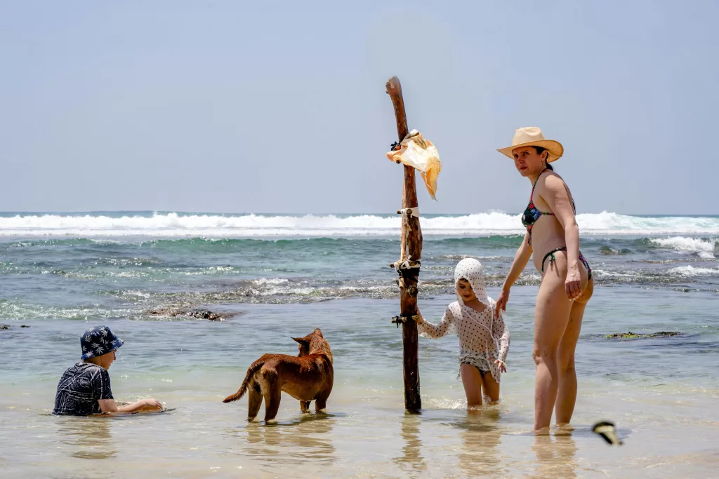 A family with a dog enjoys a sunny day on a beach in Dambulla, Sri Lanka.